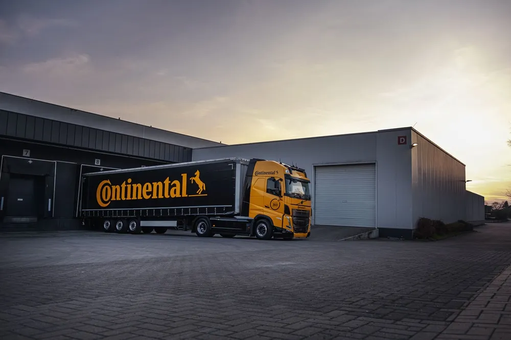 Continental branded lorry in black and yellow parked outside a depot with a gray sky