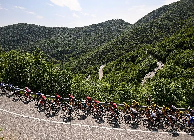 Lots of cyclists on a road above a forested valley in Italy