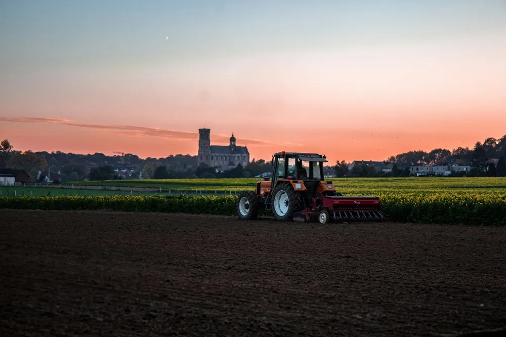 Tractor in a field during sunset with a church in the background - Photo by Nicolas Veithen