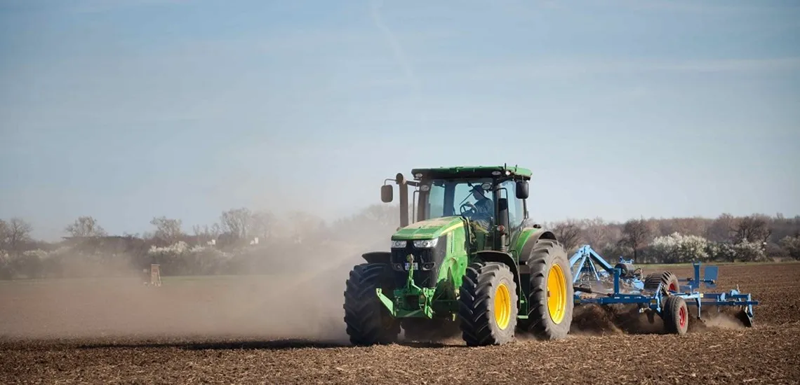 Green tractor ploughing a field front view