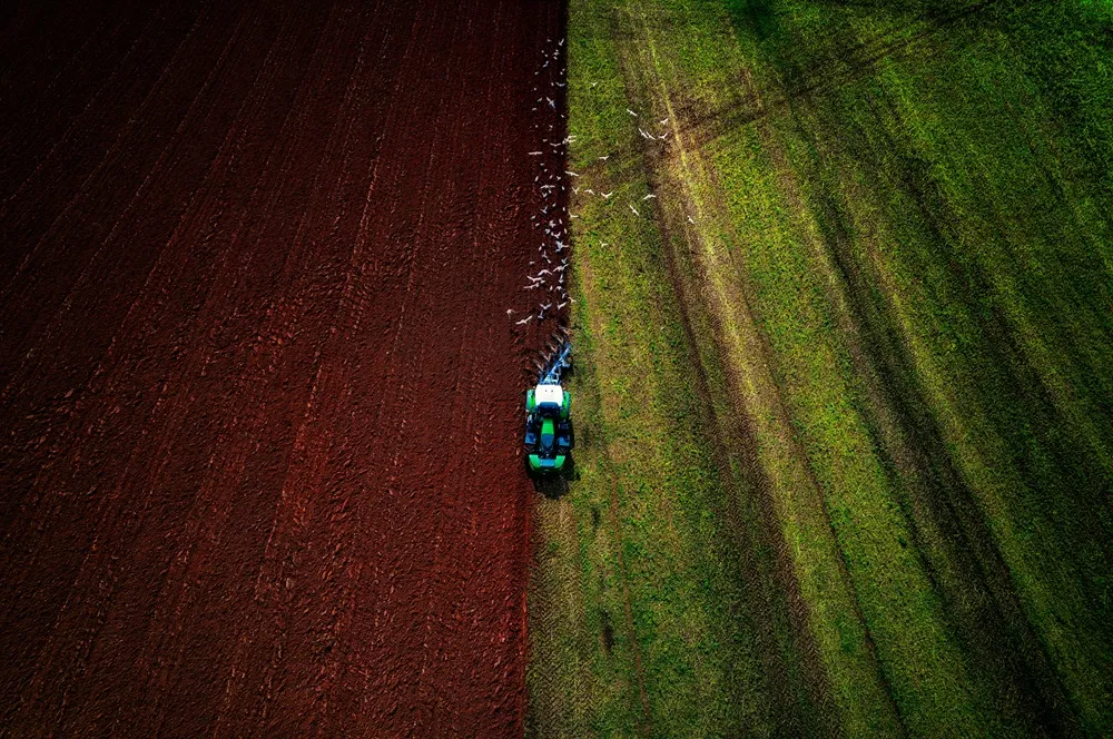 View of a green tractor ploughing a field from above