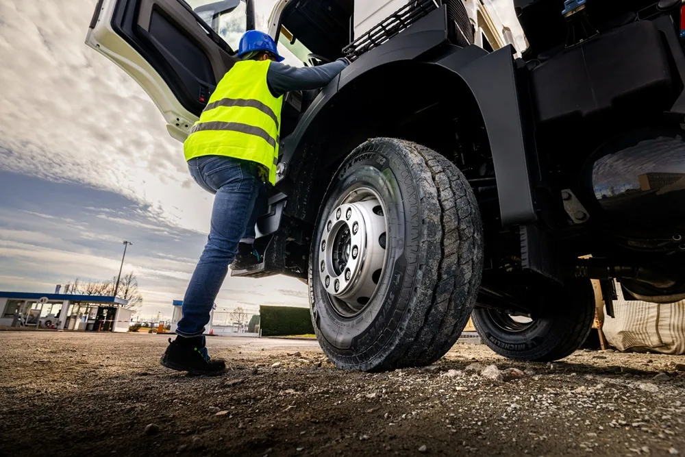 Man in high vis climbing into a lorry parked on a dirt road