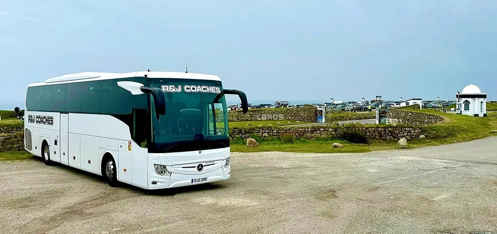 Image of a white R&J coach parked wtih greenery in the background