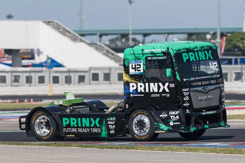 Image of racing truck from the side on a track in black with PRINX sponsership in teal green
