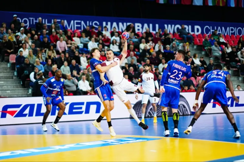 Image of a men's handball tournement with players wearing blue and whte kits with a crwod in the background
