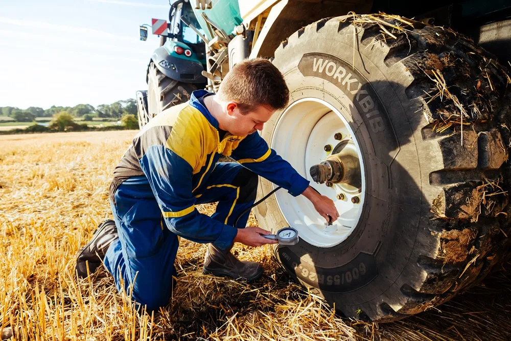 Image of a farmer checking the pressure on his tractor's trailer tyre in a field